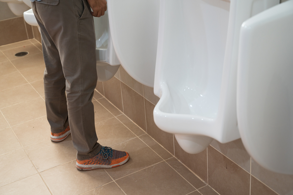 A man standing and urinating at urinal.