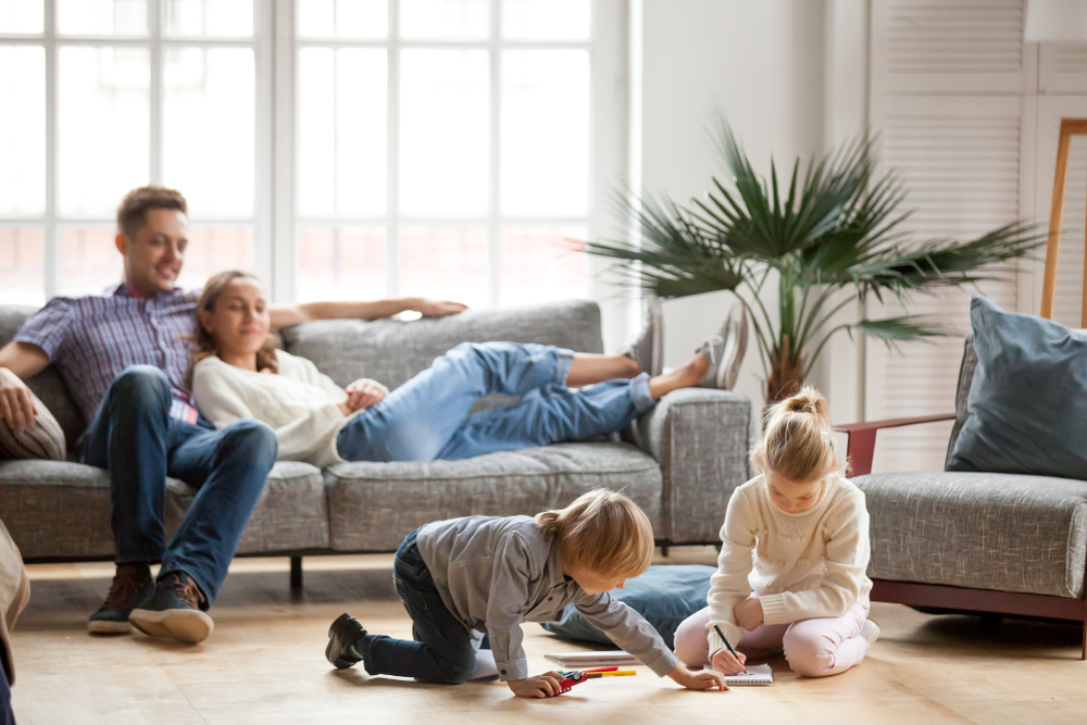 man and wife sitting on the couch while they watch their children play